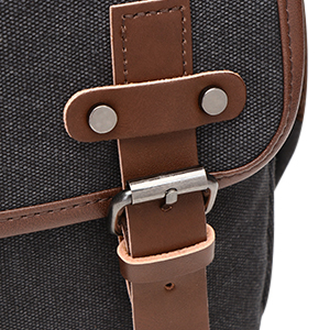 Nahaufnahme der Riemenbefestigung einer Tasche, die dunkles Leinenmaterial mit braunem Lederbesatz und Metallschnallenverschluss zeigt