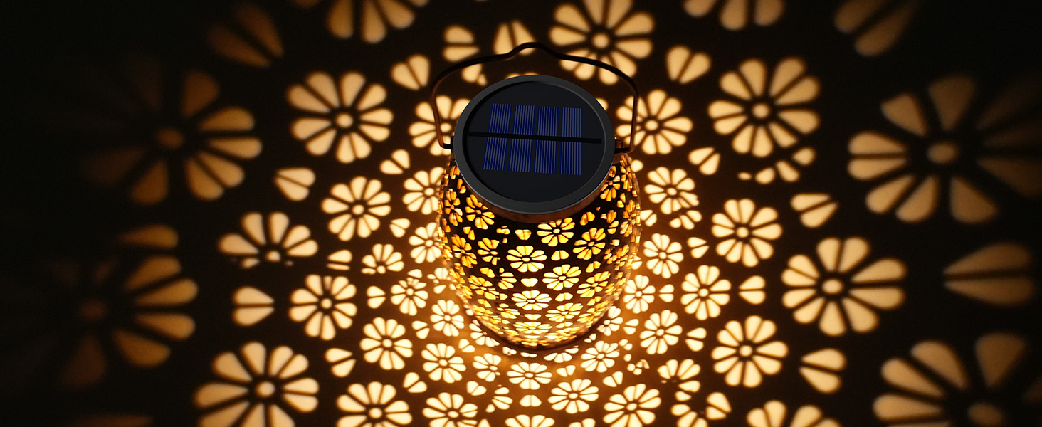 Solarbetriebene Laterne mit filigranem Blumenmuster, das warmes Licht ausstrahlt und dekorative Schatten wirft. Blaues Solarpanel
