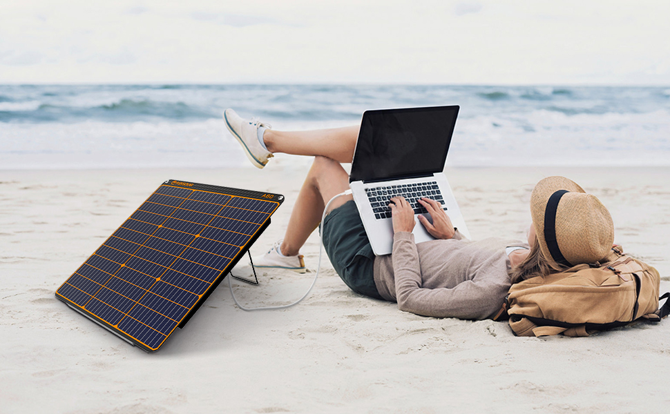 eine Frau liegt mit einem Laptop am Strand.